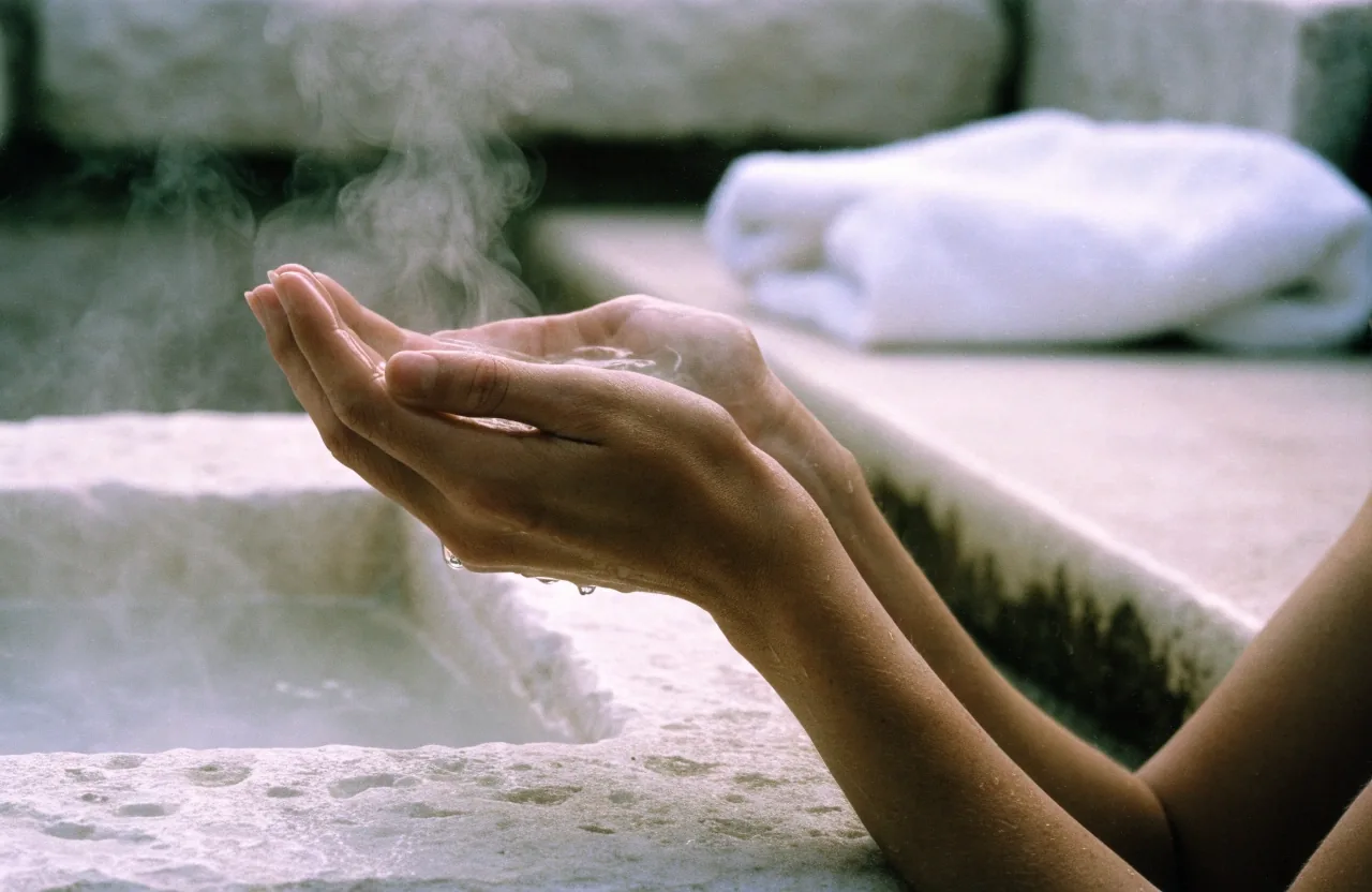 Hand scooping warm mineral water from a stone basin at a thermal spa